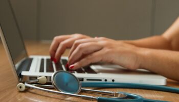 person sitting while using laptop computer and green stethoscope near